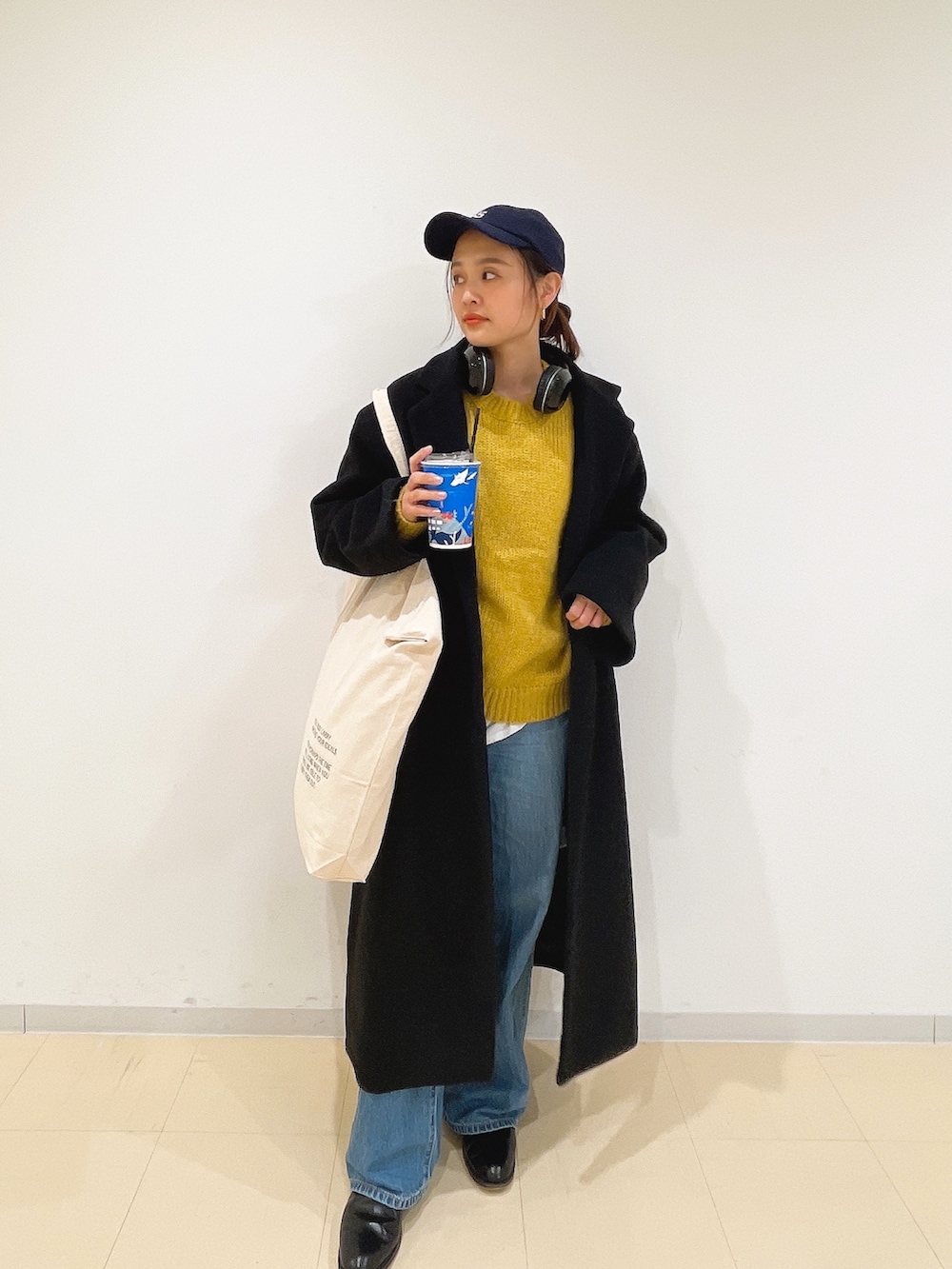 イエロー系のニット/セーター、ホワイト系のハンドバッグ、ブルー系のデニムパンツを着用したレディースの冬コーディネートの4枚目の写真