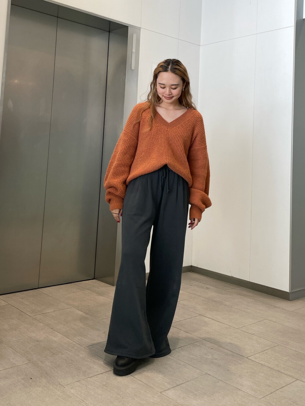 オレンジ系のニット/セーター、グレー系のスウェットパンツを着用したレディースの秋コーディネートの3枚目の写真