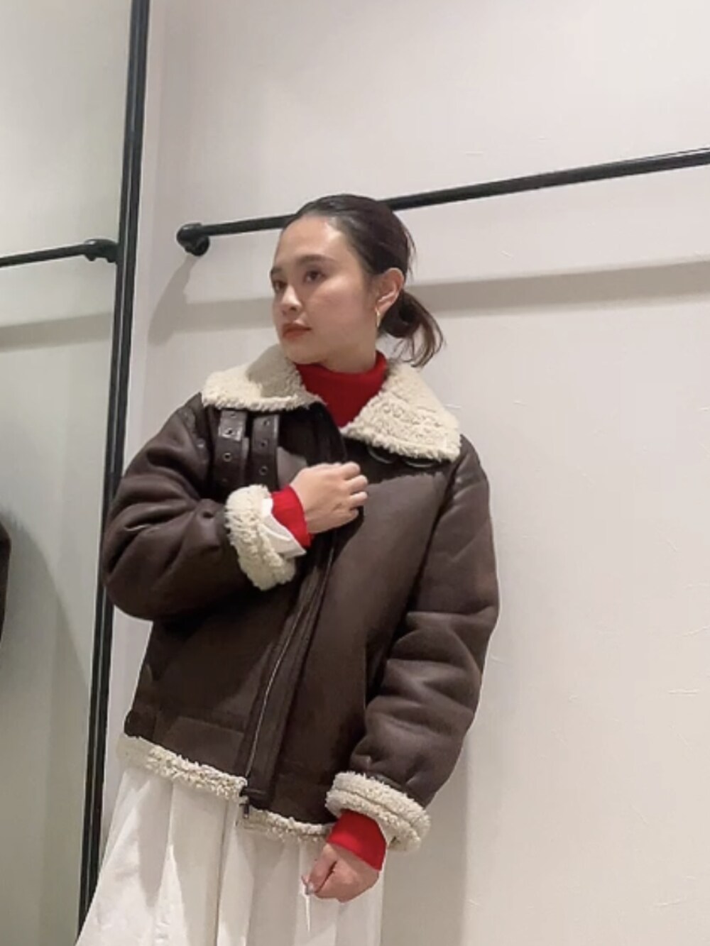 ブラウン系のムートンコート、レッド系のニット/セーター、ブラック系のワンピースを着用したレディースの冬コーディネートの4枚目の写真