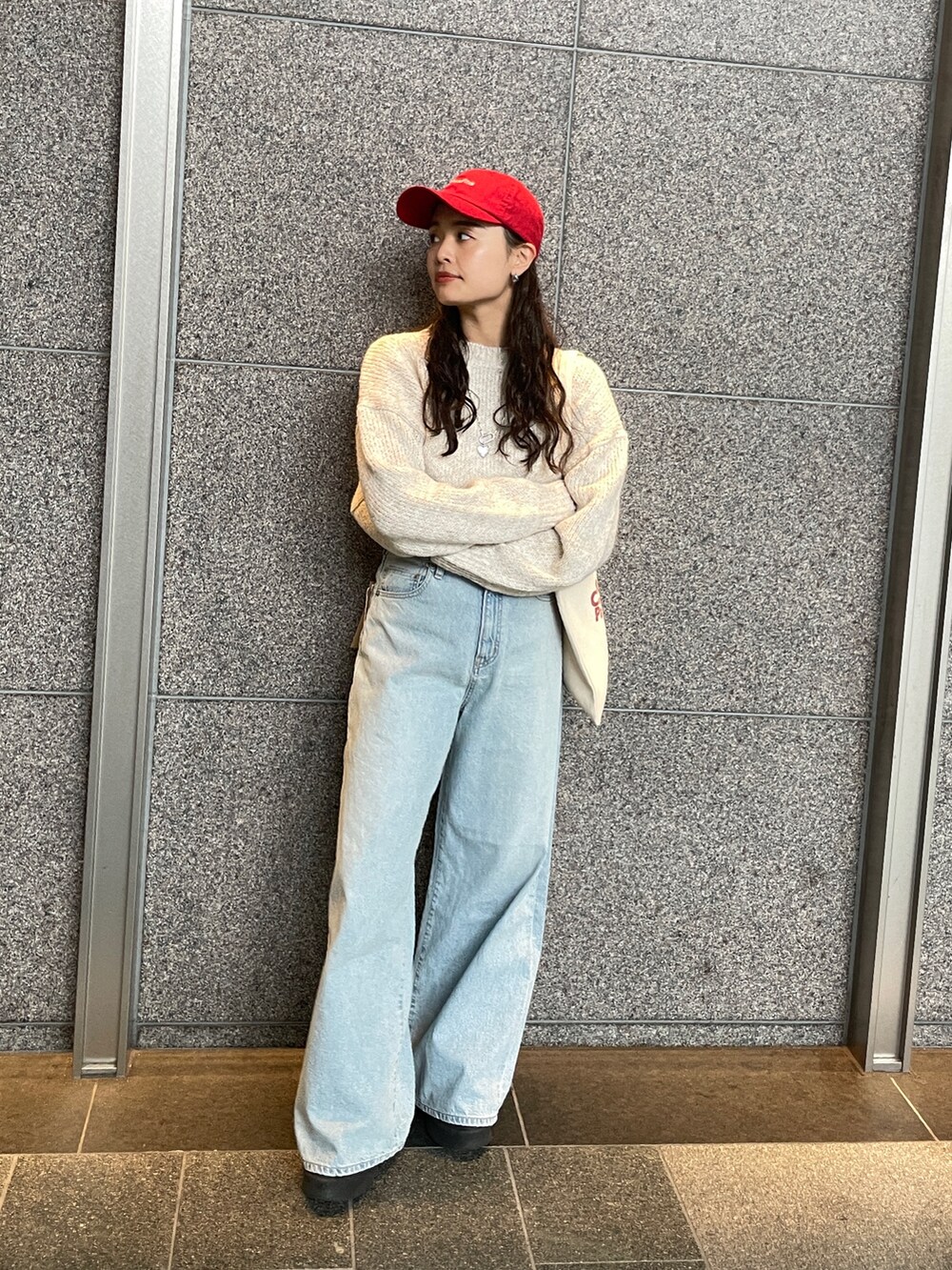 ブルー系のデニムパンツ、ホワイト系のニット/セーター、レッド系のトートバッグを着用したレディースの秋コーディネートの3枚目の写真