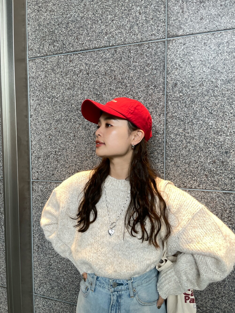 ブルー系のデニムパンツ、ホワイト系のニット/セーター、レッド系のトートバッグを着用したレディースの秋コーディネートの5枚目の写真