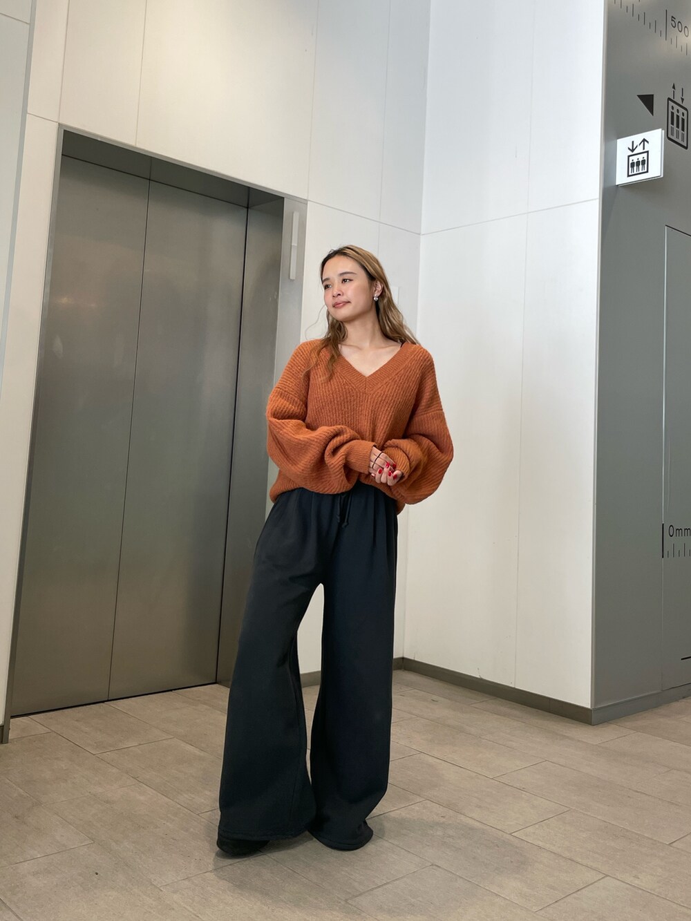 オレンジ系のニット/セーター、グレー系のスウェットパンツを着用したレディースの秋コーディネートの2枚目の写真