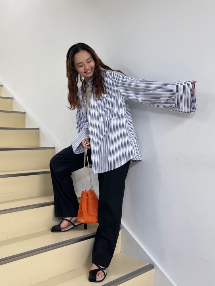 ブラック系のその他パンツ、ブルー系のシャツ/ブラウス、オレンジ系のハンドバッグを着用したレディースの春コーディネートの2枚目の写真