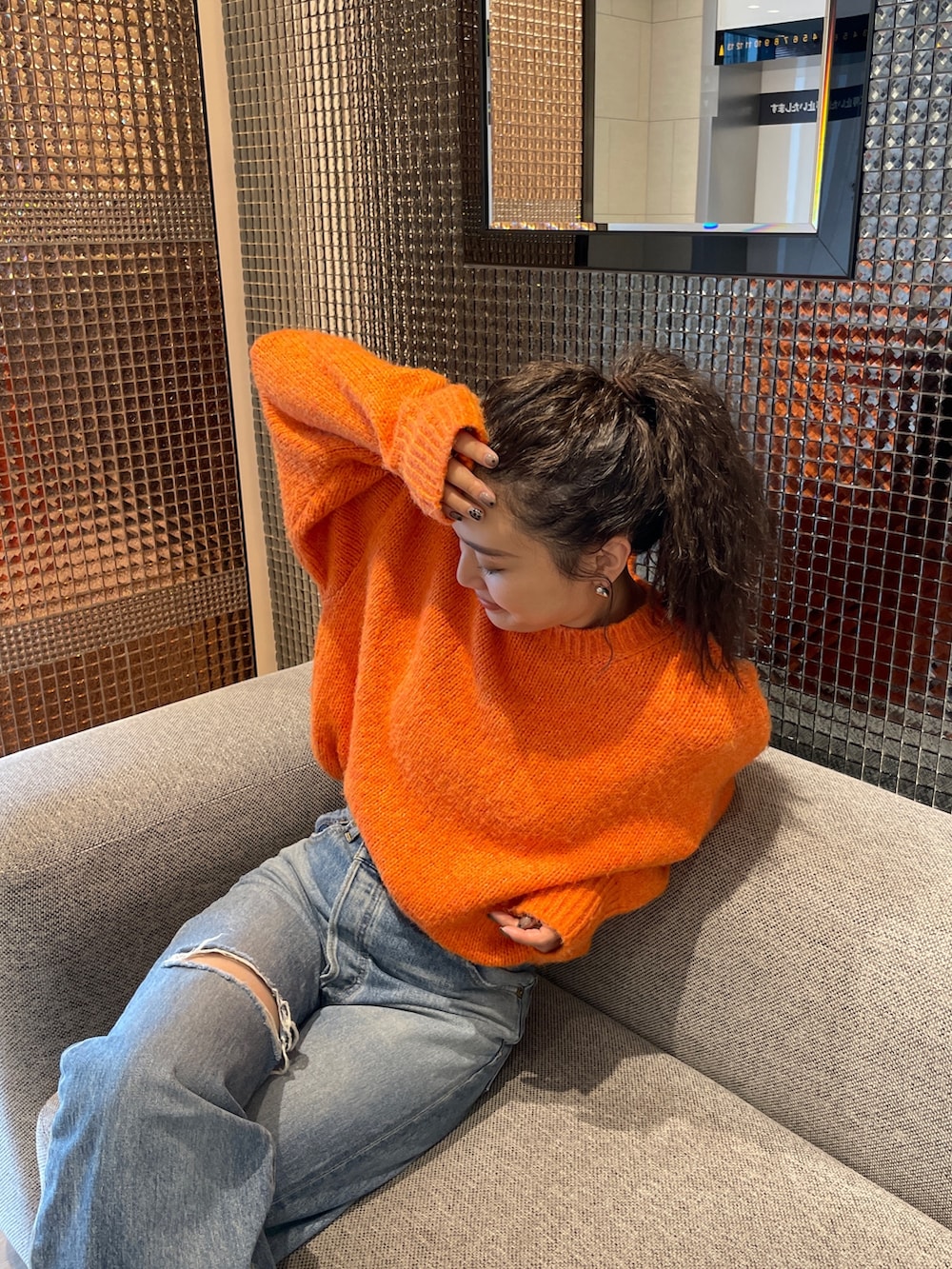 ブルー系のデニムパンツ、ブラック系のブーツ、オレンジ系のニット/セーターを着用したレディースの秋コーディネートの3枚目の写真