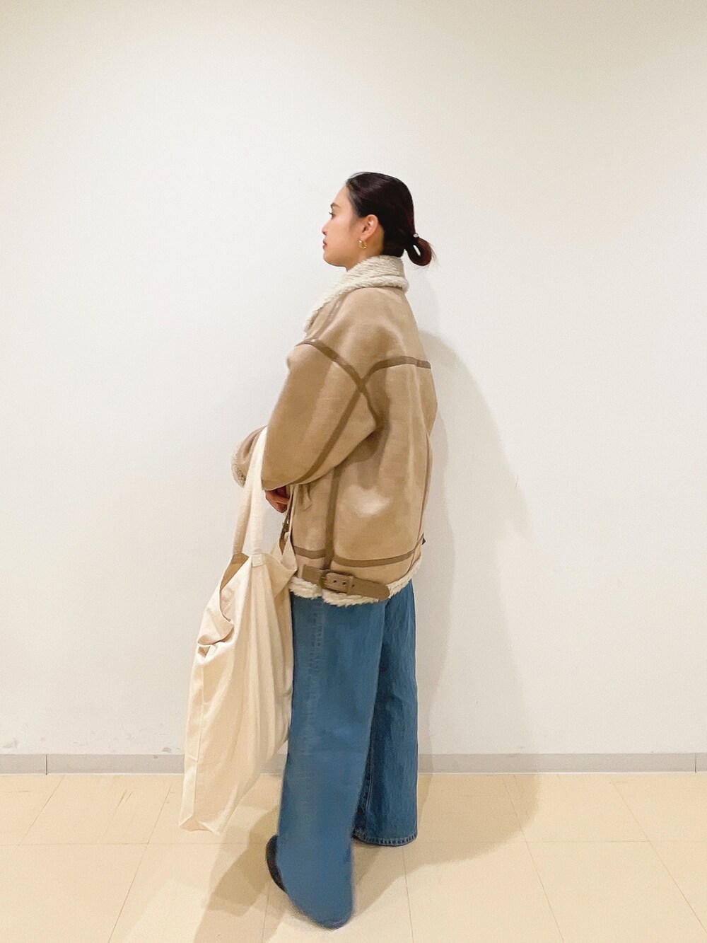 ベージュ系のムートンコート、ブルー系のニット/セーター、ホワイト系のハンドバッグを着用したレディースの冬コーディネートの4枚目の写真