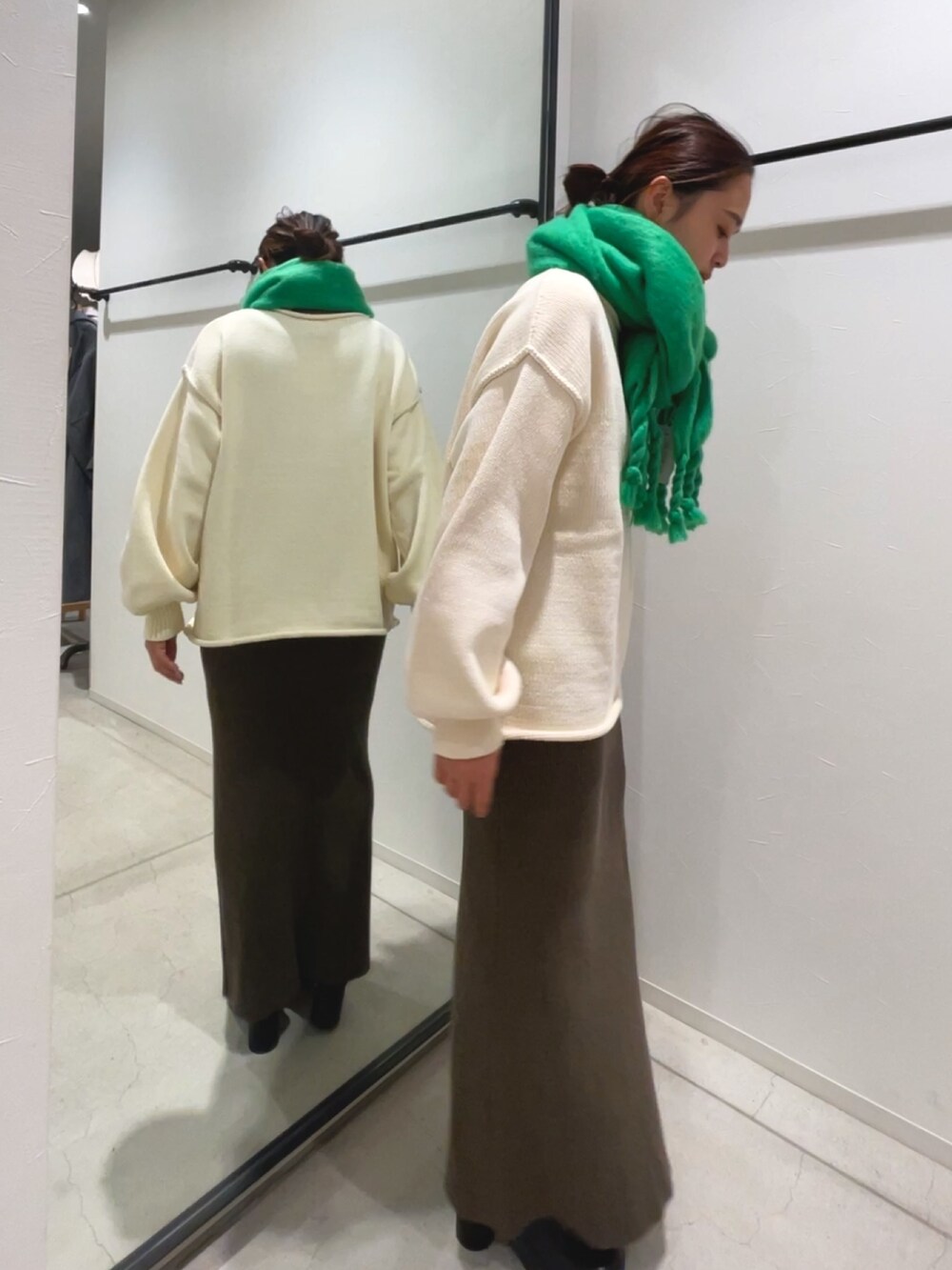 グレー系のスカート、ホワイト系のニット/セーター、グリーン系のマフラーを着用したレディースの冬コーディネートの2枚目の写真