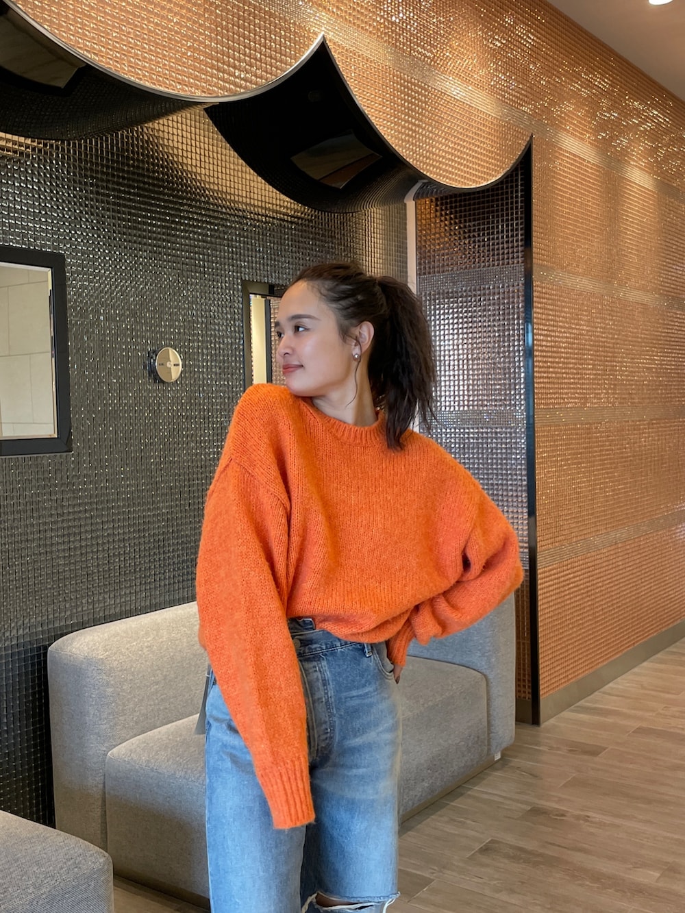 ブルー系のデニムパンツ、ブラック系のブーツ、オレンジ系のニット/セーターを着用したレディースの秋コーディネートの9枚目の写真