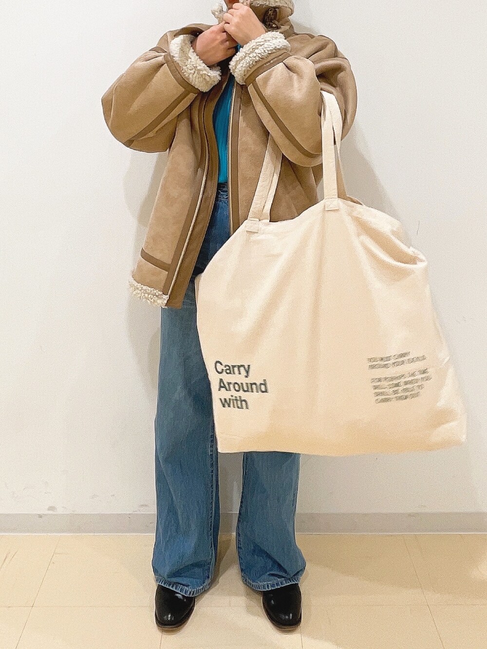 ベージュ系のムートンコート、ブルー系のニット/セーター、ホワイト系のハンドバッグを着用したレディースの冬コーディネートの3枚目の写真