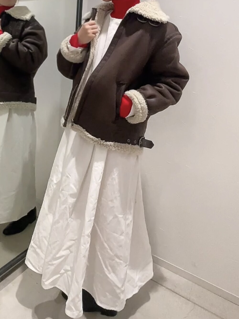 ブラウン系のムートンコート、レッド系のニット/セーター、ブラック系のワンピースを着用したレディースの冬コーディネートの2枚目の写真