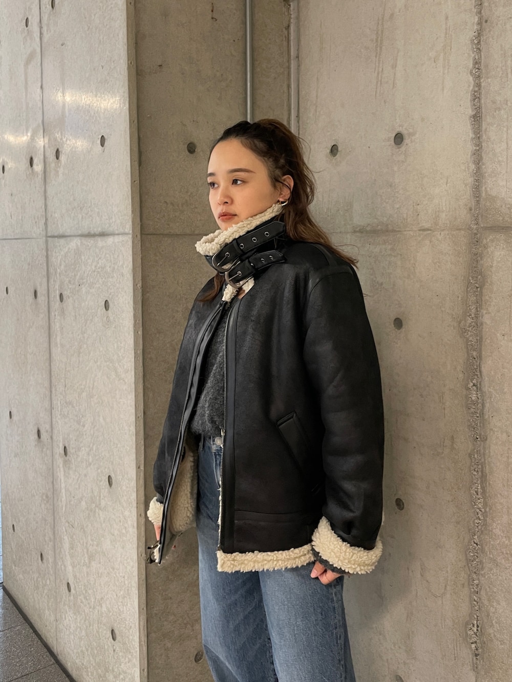 ブラック系のムートンコート、ブルー系のデニムパンツ、グレー系のニット/セーターを着用したレディースの冬コーディネートの3枚目の写真