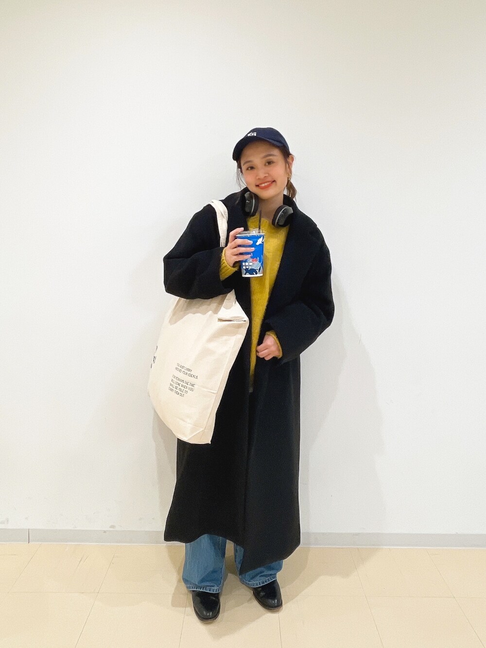 イエロー系のニット/セーター、ホワイト系のハンドバッグ、ブルー系のデニムパンツを着用したレディースの冬コーディネートの2枚目の写真