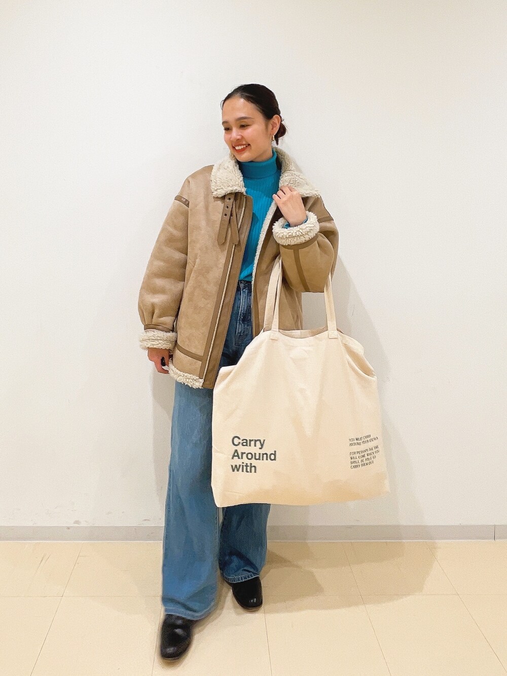 ベージュ系のムートンコート、ブルー系のニット/セーター、ホワイト系のハンドバッグを着用したレディースの冬コーディネートの2枚目の写真