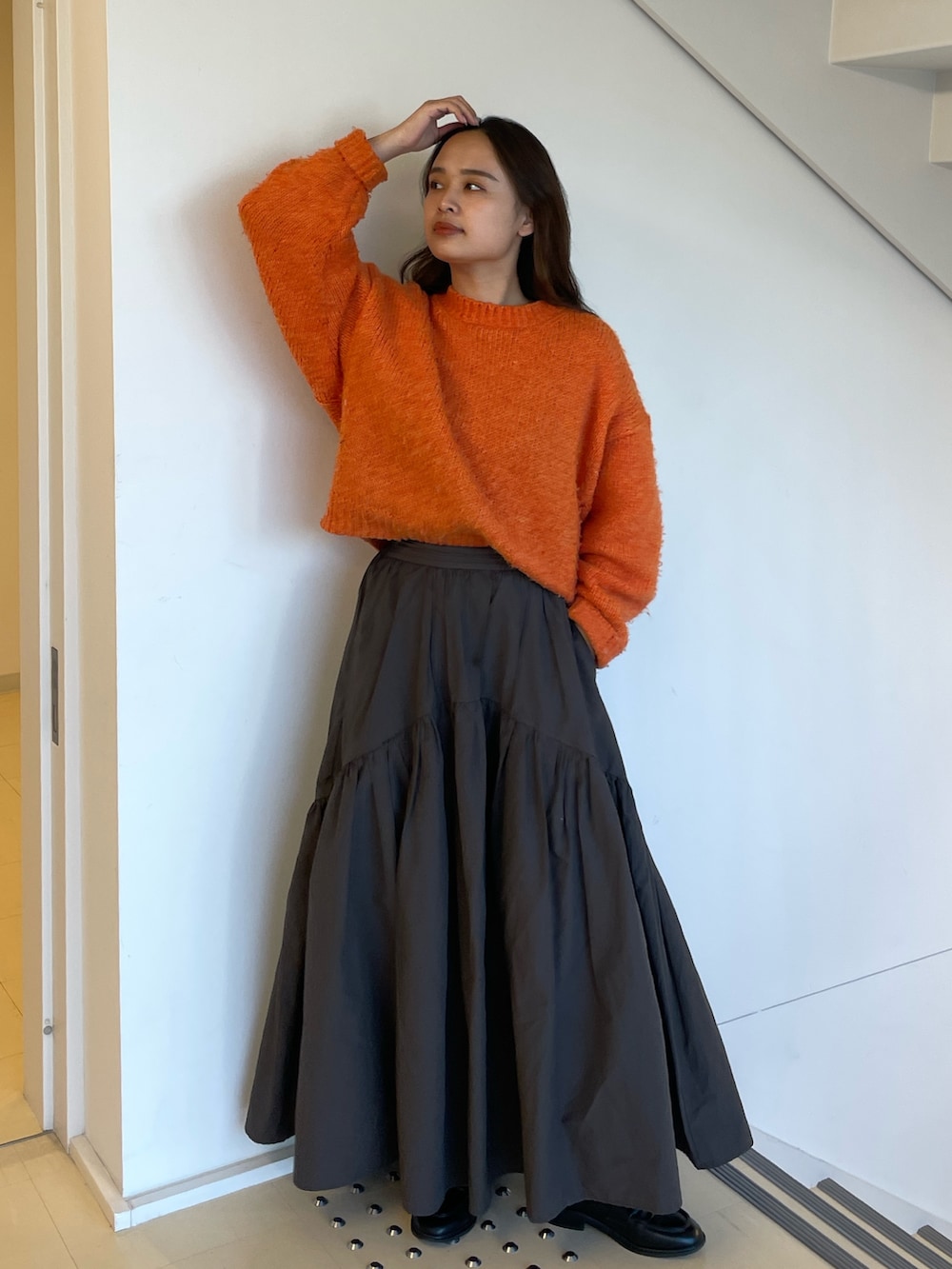 グレー系のスカート、オレンジ系のニット/セーターを着用したレディースの冬コーディネートの2枚目の写真