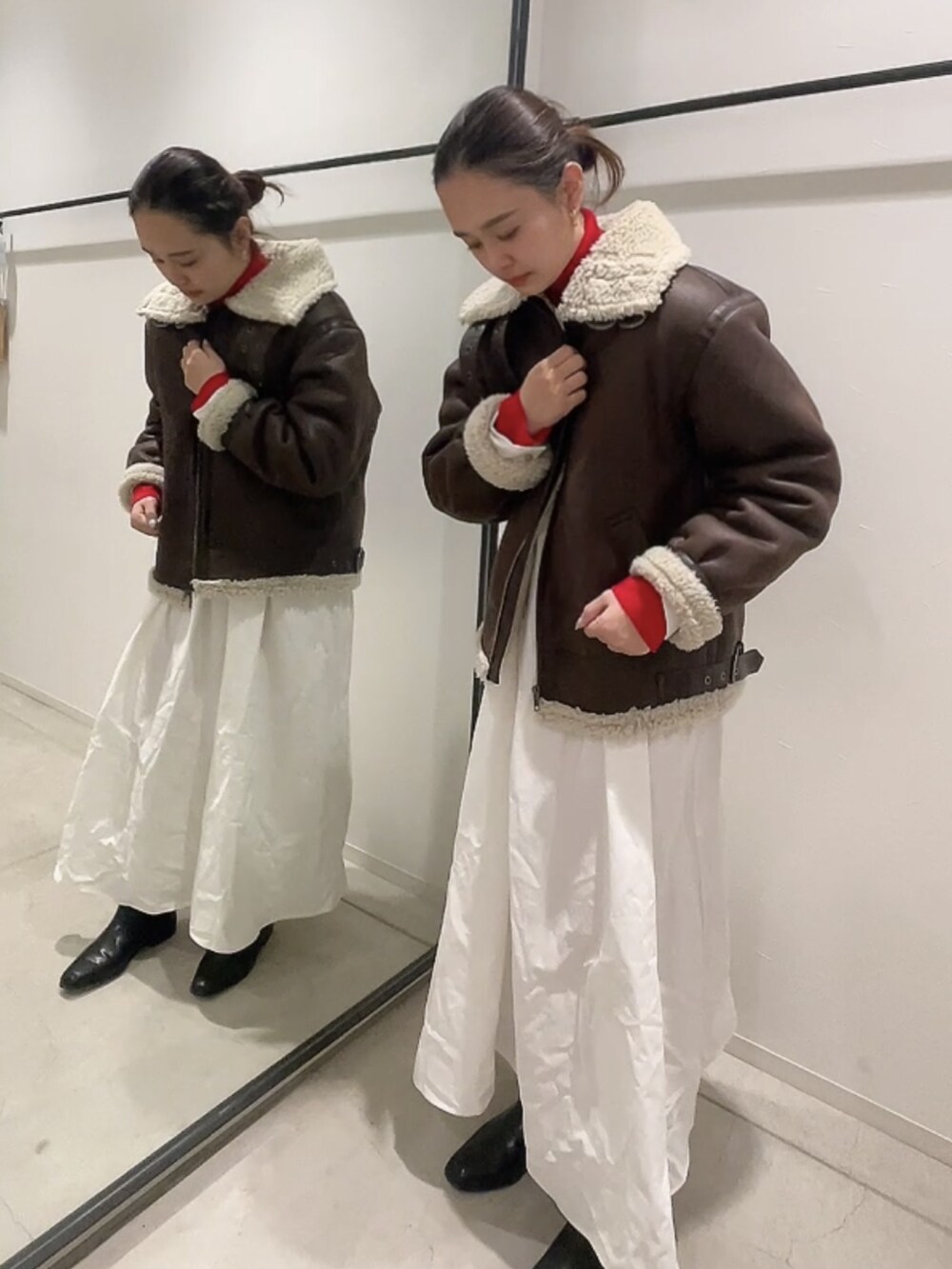 ブラウン系のムートンコート、レッド系のニット/セーター、ブラック系のワンピースを着用したレディースの冬コーディネートの3枚目の写真