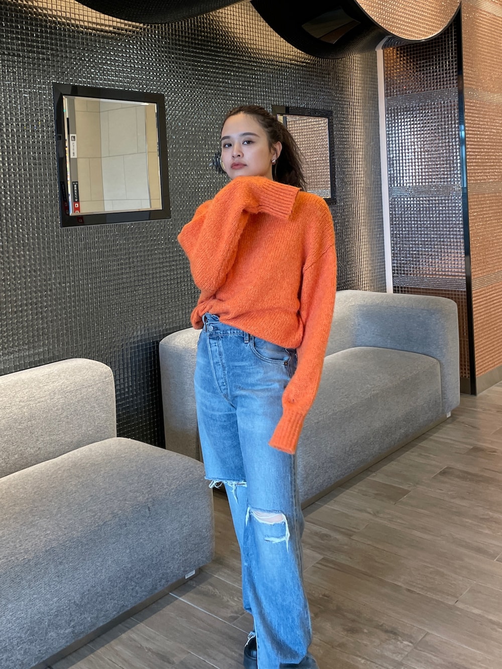 ブルー系のデニムパンツ、ブラック系のブーツ、オレンジ系のニット/セーターを着用したレディースの秋コーディネートの2枚目の写真