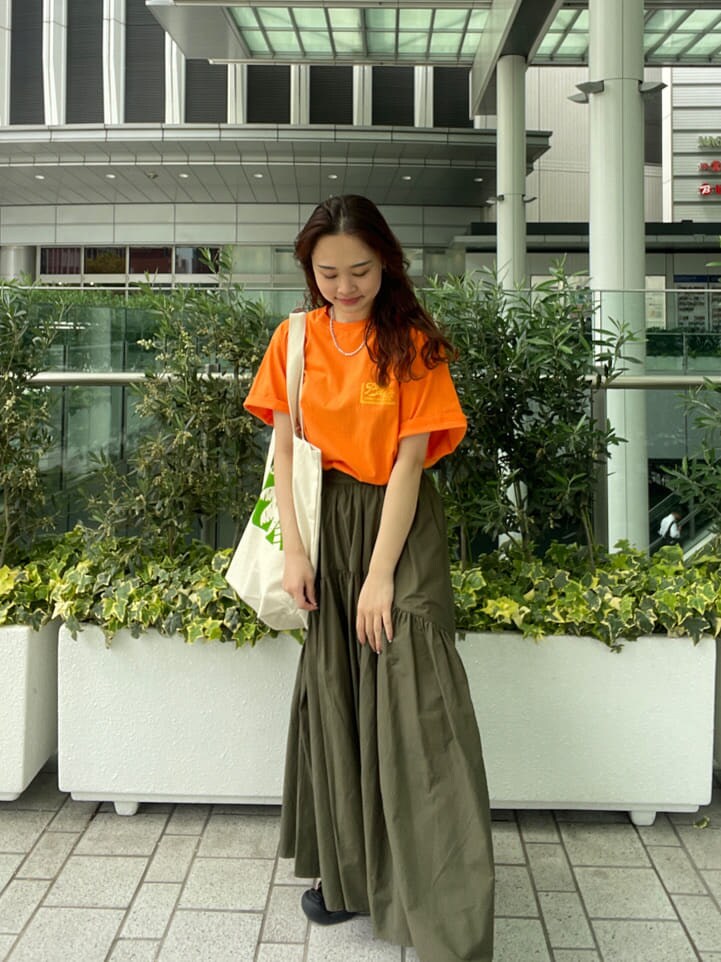 ベージュ系のスカート、オレンジ系のTシャツ/カットソー、グリーン系のハンドバッグを着用したレディースの春コーディネートの2枚目の写真