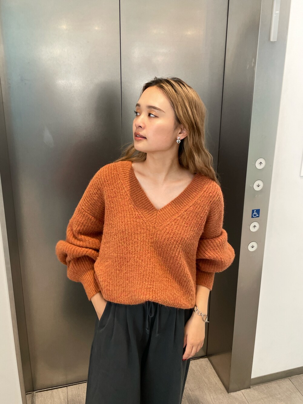 オレンジ系のニット/セーター、グレー系のスウェットパンツを着用したレディースの秋コーディネートの4枚目の写真