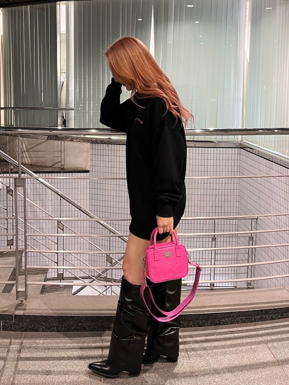 ブラック系のスウェット、ピンク系のショルダーバッグ、ブラック系のブーツを着用したレディースの冬コーディネートの3枚目の写真