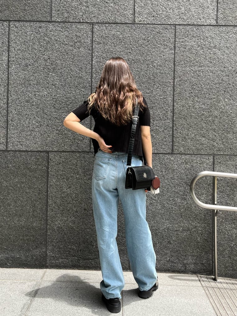 ブラック系のショルダーバッグ、ブルー系のデニムパンツ、ブラック系のニット/セーターを着用したレディースの夏コーディネートの2枚目の写真