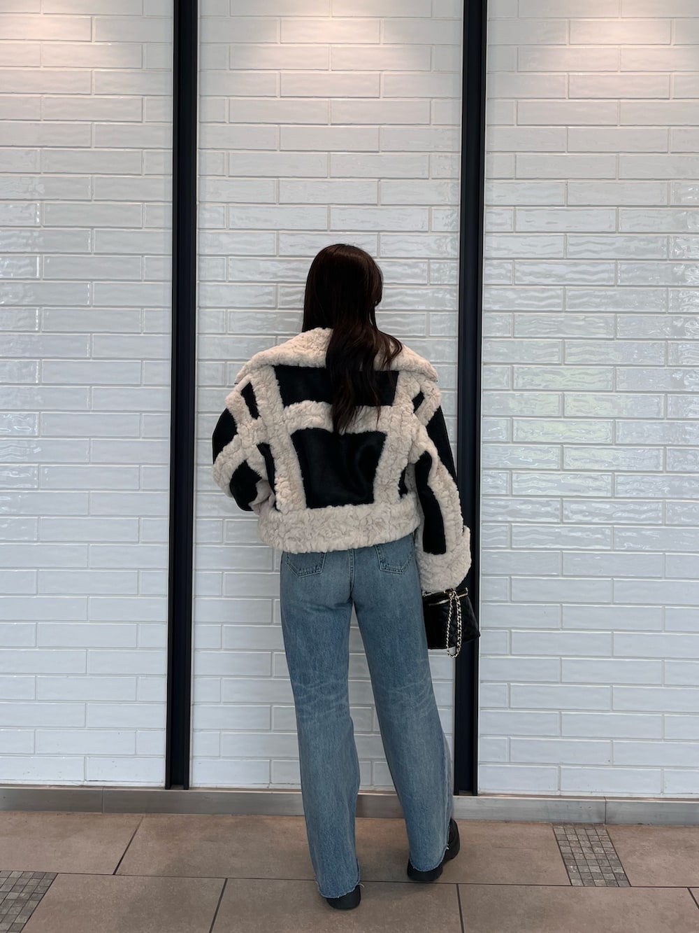 ブラック系のムートンコート、ブルー系のニット/セーター、ブルー系のデニムパンツを着用したレディースの夏コーディネートの2枚目の写真