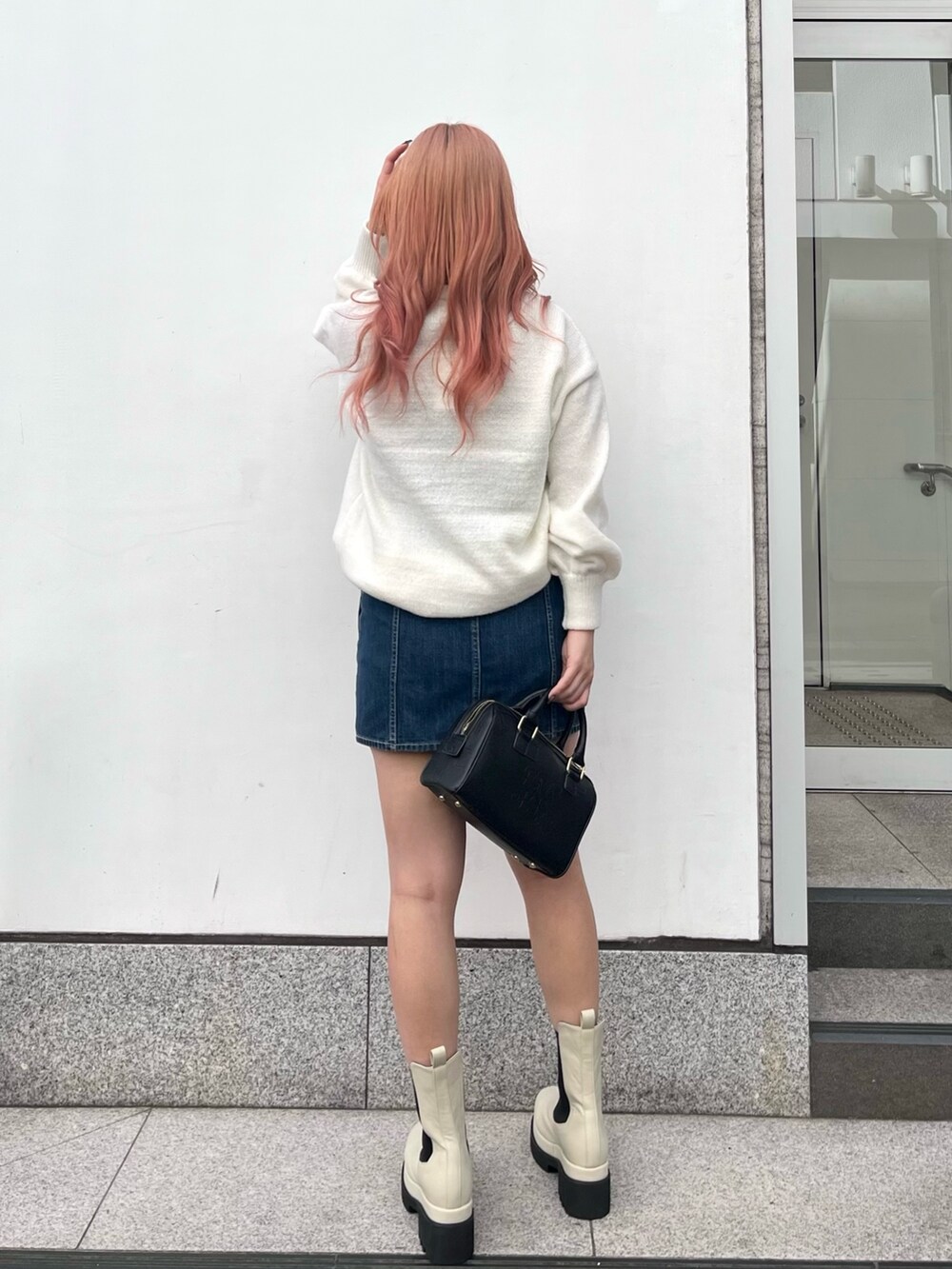 ホワイト系のニット/セーター、ブルー系のデニムスカート、ブラック系のボストンバッグを着用したレディースの冬コーディネートの2枚目の写真