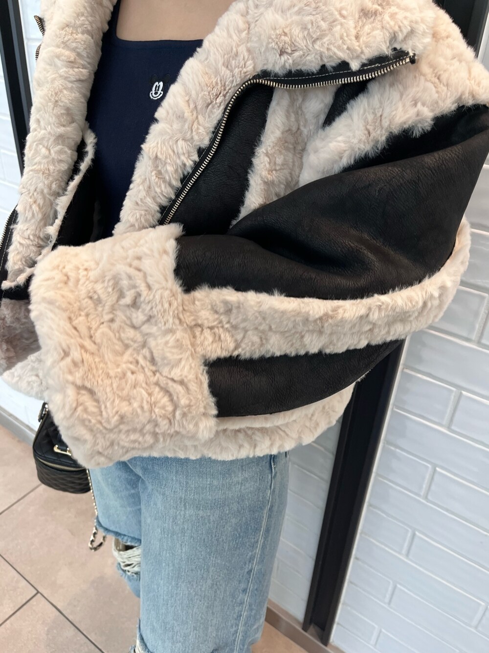 ブラック系のムートンコート、ブルー系のニット/セーター、ブルー系のデニムパンツを着用したレディースの夏コーディネートの5枚目の写真