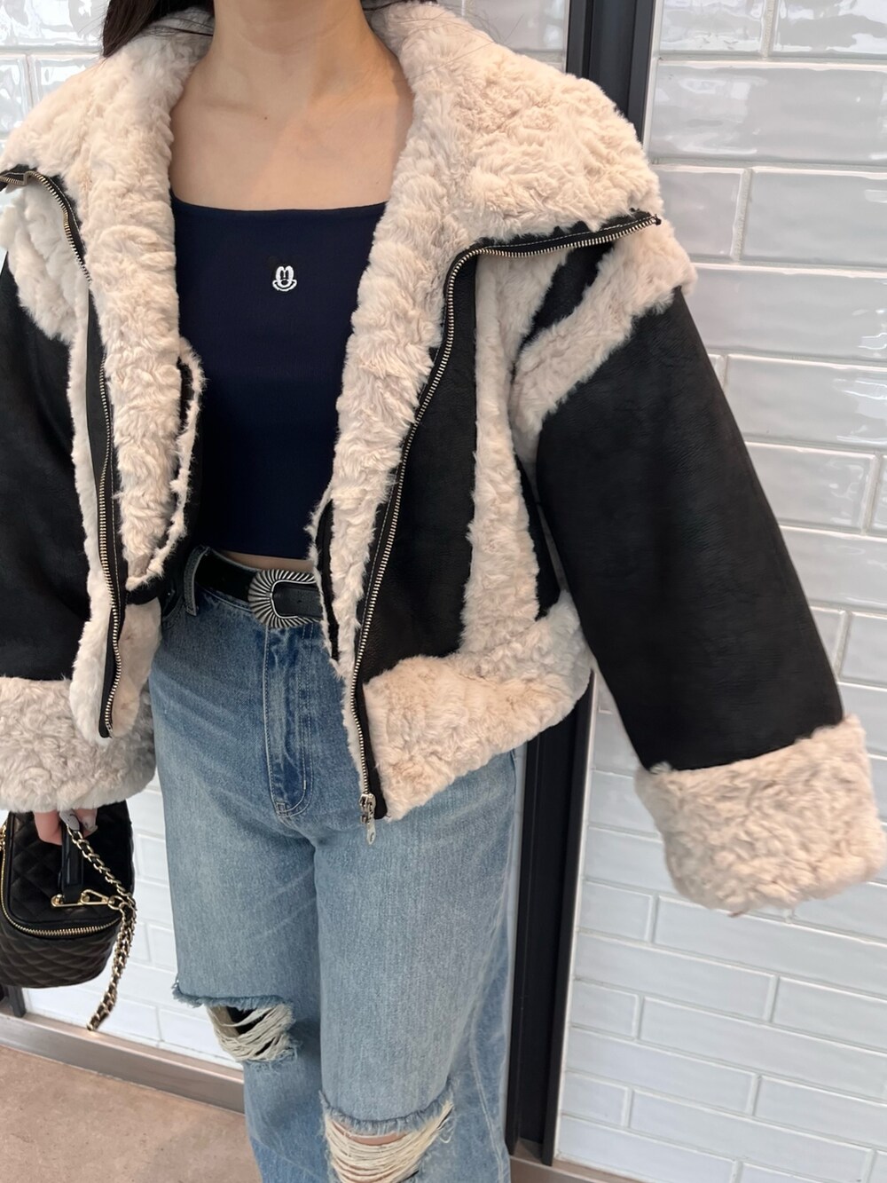 ブラック系のムートンコート、ブルー系のニット/セーター、ブルー系のデニムパンツを着用したレディースの夏コーディネートの4枚目の写真