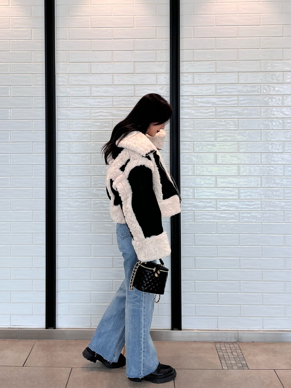 ブラック系のムートンコート、ブルー系のニット/セーター、ブルー系のデニムパンツを着用したレディースの夏コーディネートの3枚目の写真