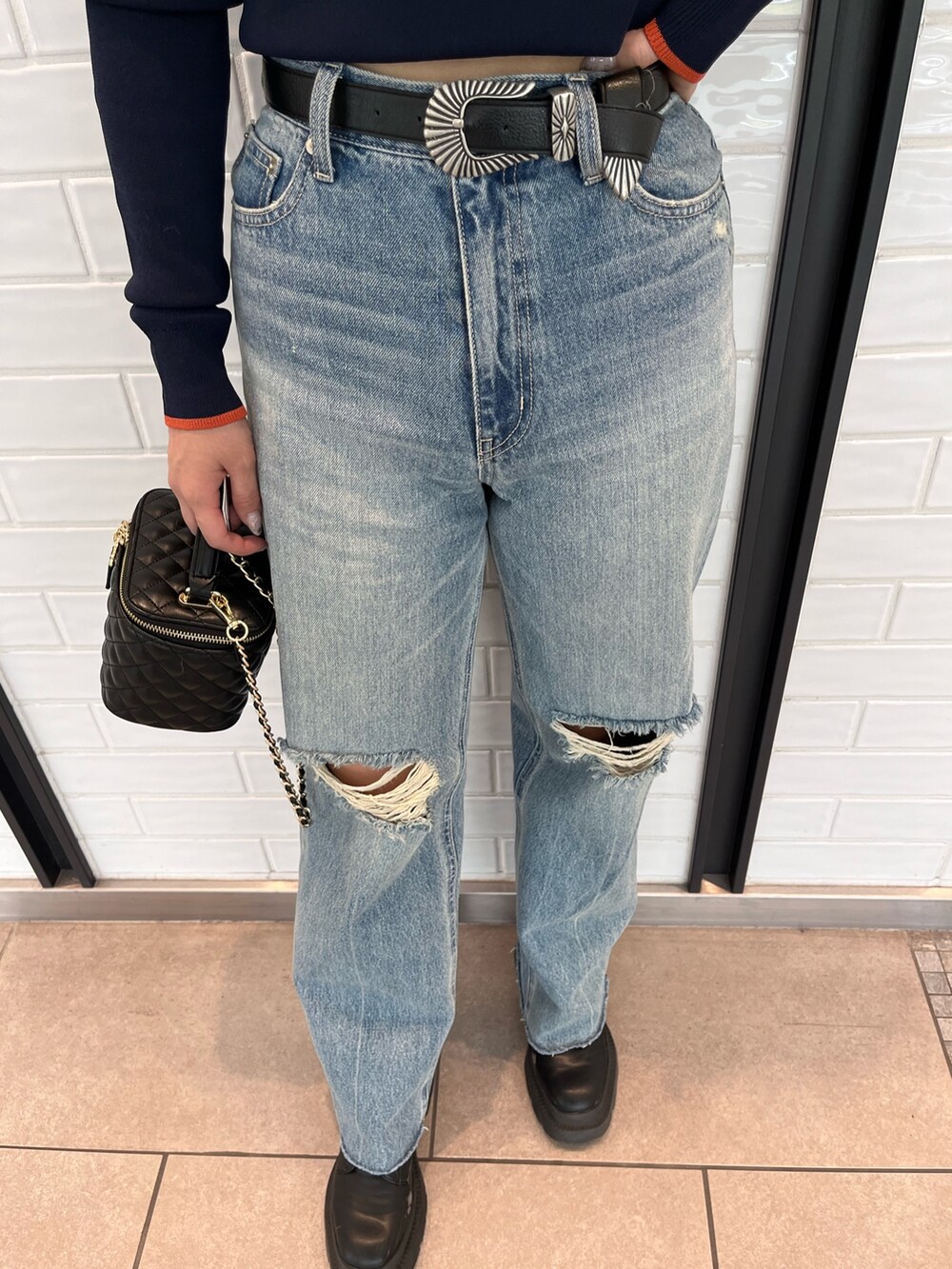 ブラック系のムートンコート、ブルー系のニット/セーター、ブルー系のデニムパンツを着用したレディースの夏コーディネートの7枚目の写真