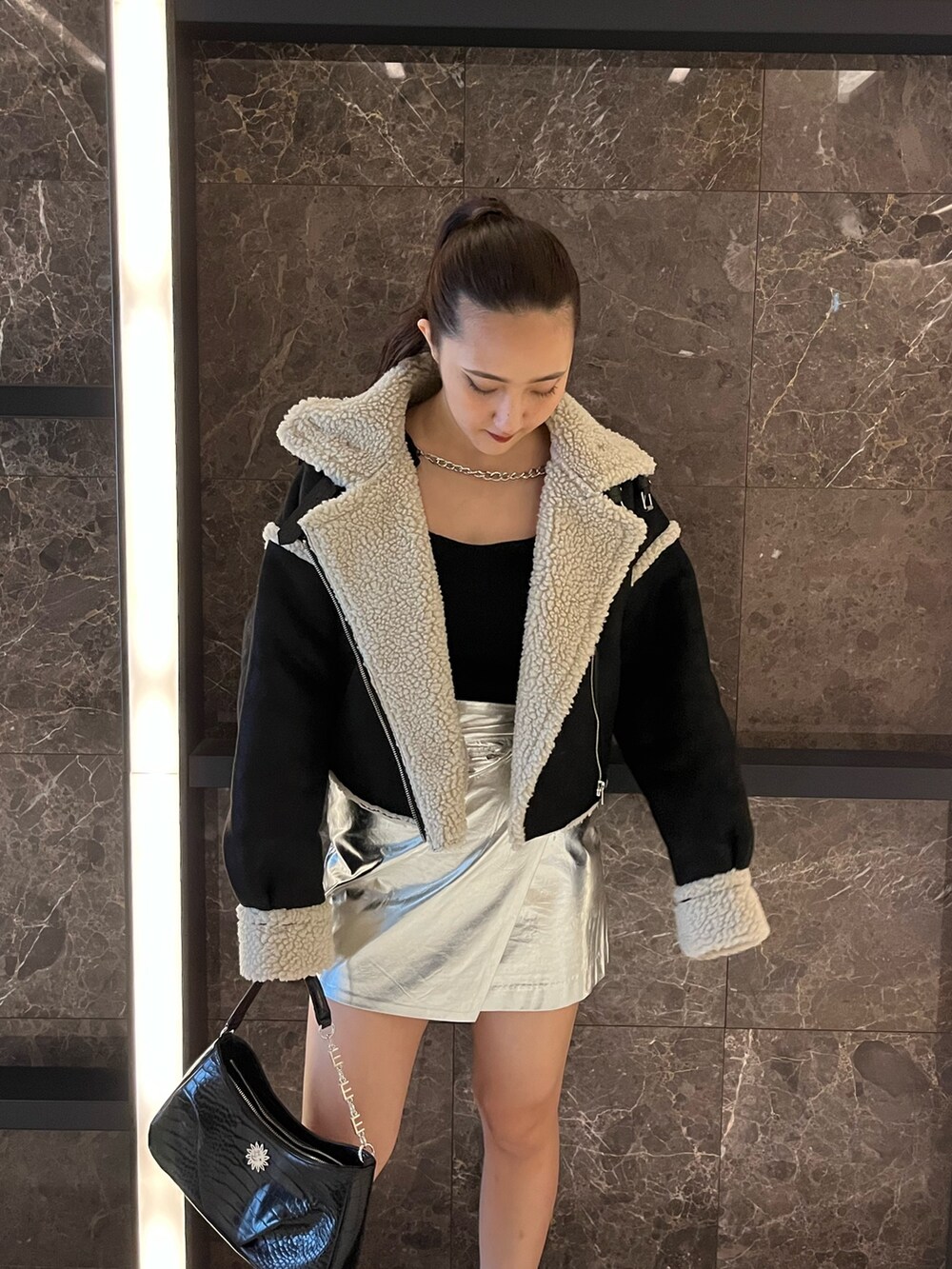ブラック系のムートンコート、ブラック系のニット/セーター、シルバー系のスカートを着用したレディースの秋コーディネートの4枚目の写真