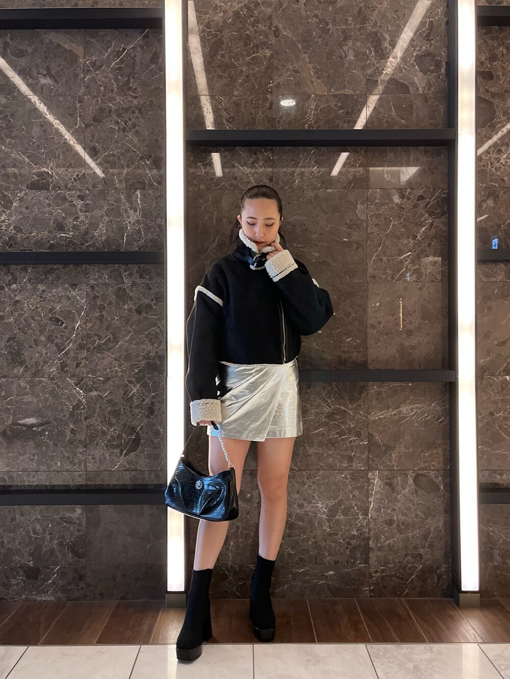 ブラック系のムートンコート、ブラック系のニット/セーター、シルバー系のスカートを着用したレディースの秋コーディネートの3枚目の写真