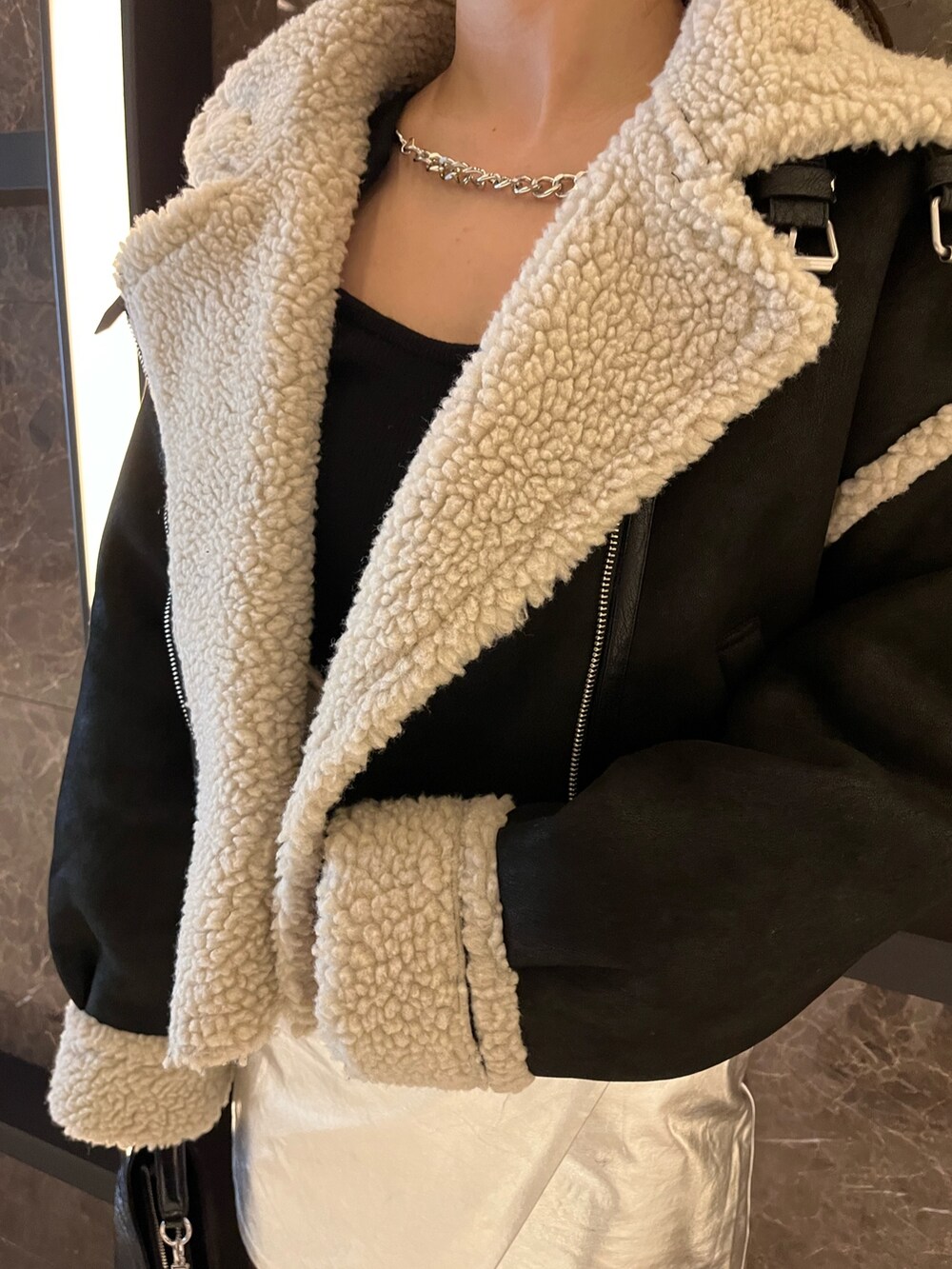 ブラック系のムートンコート、ブラック系のニット/セーター、シルバー系のスカートを着用したレディースの秋コーディネートの5枚目の写真