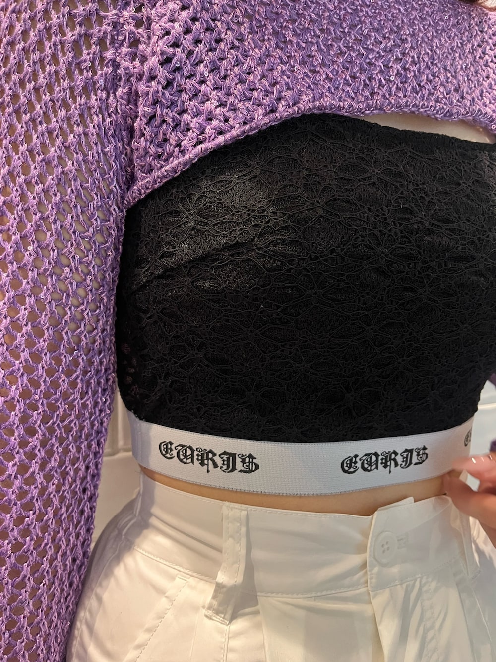 パープル系のニット/セーター、ブラック系のキャミソール、ブラック系のショルダーバッグを着用したレディースの春コーディネートの5枚目の写真