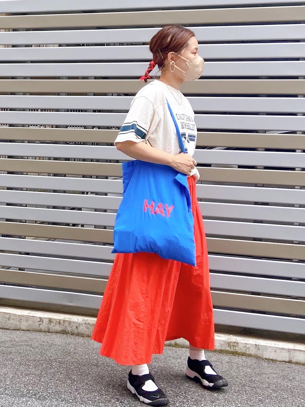 ブラック系のスニーカー、オレンジ系のスカート、ベージュ系のTシャツ/カットソーを着用したレディースの夏コーディネートの2枚目の写真