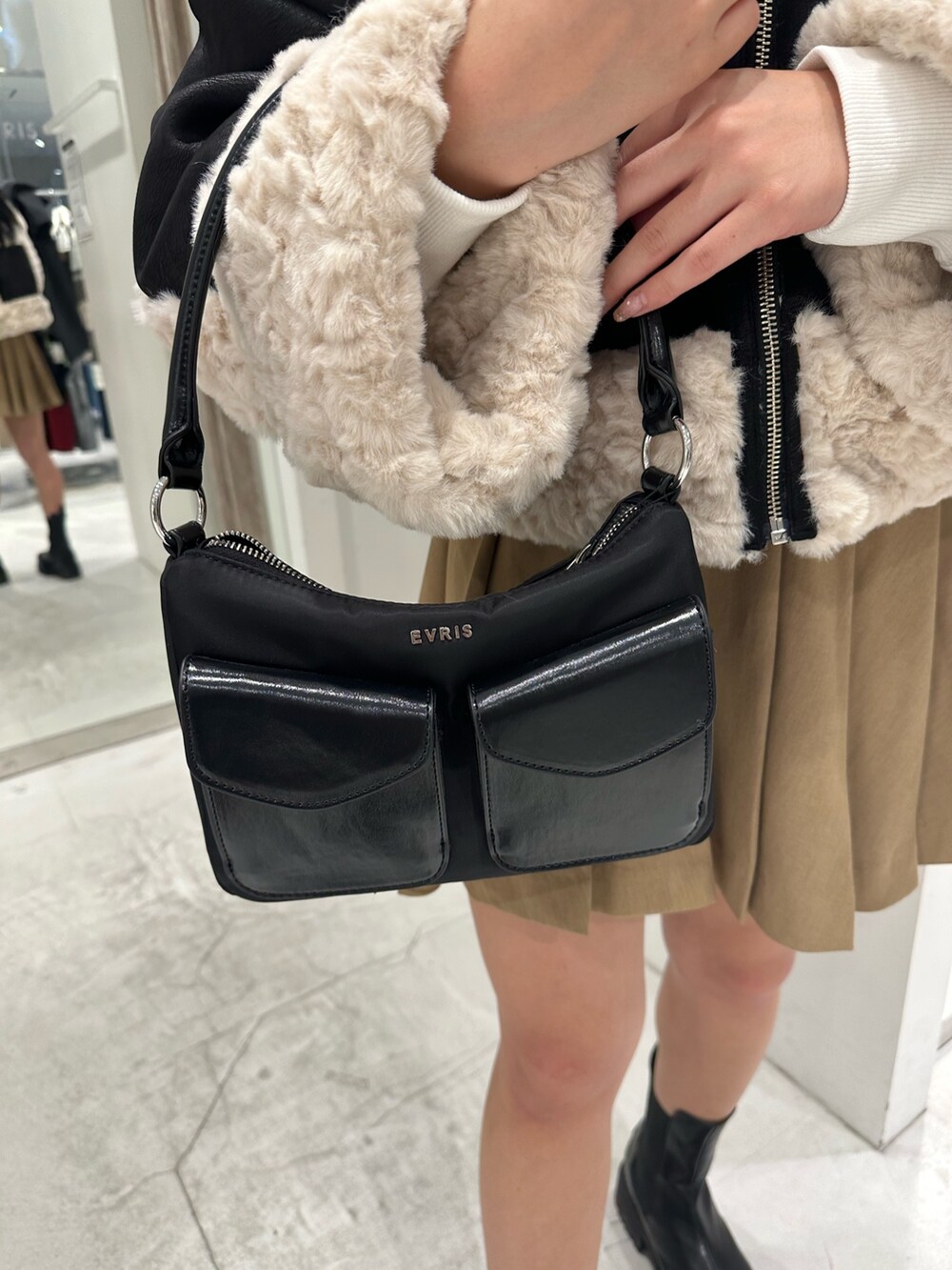 ブラック系のムートンコート、ベージュ系のスカート、ブラック系のハンドバッグを着用したレディースの冬コーディネートの9枚目の写真