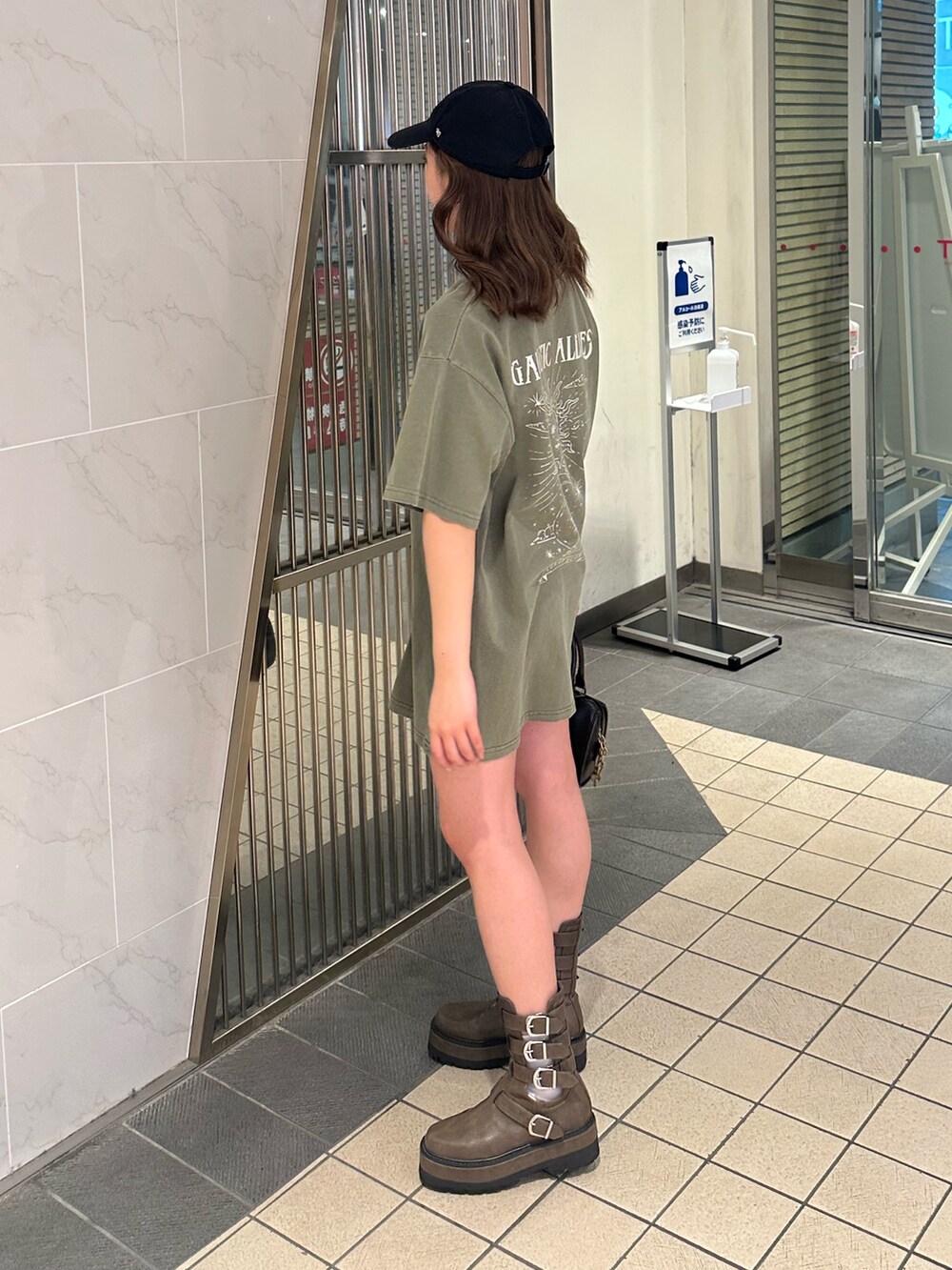 ブラック系のショルダーバッグ、ブラウン系のブーツ、グリーン系のTシャツ/カットソーを着用したレディースの春コーディネートの2枚目の写真