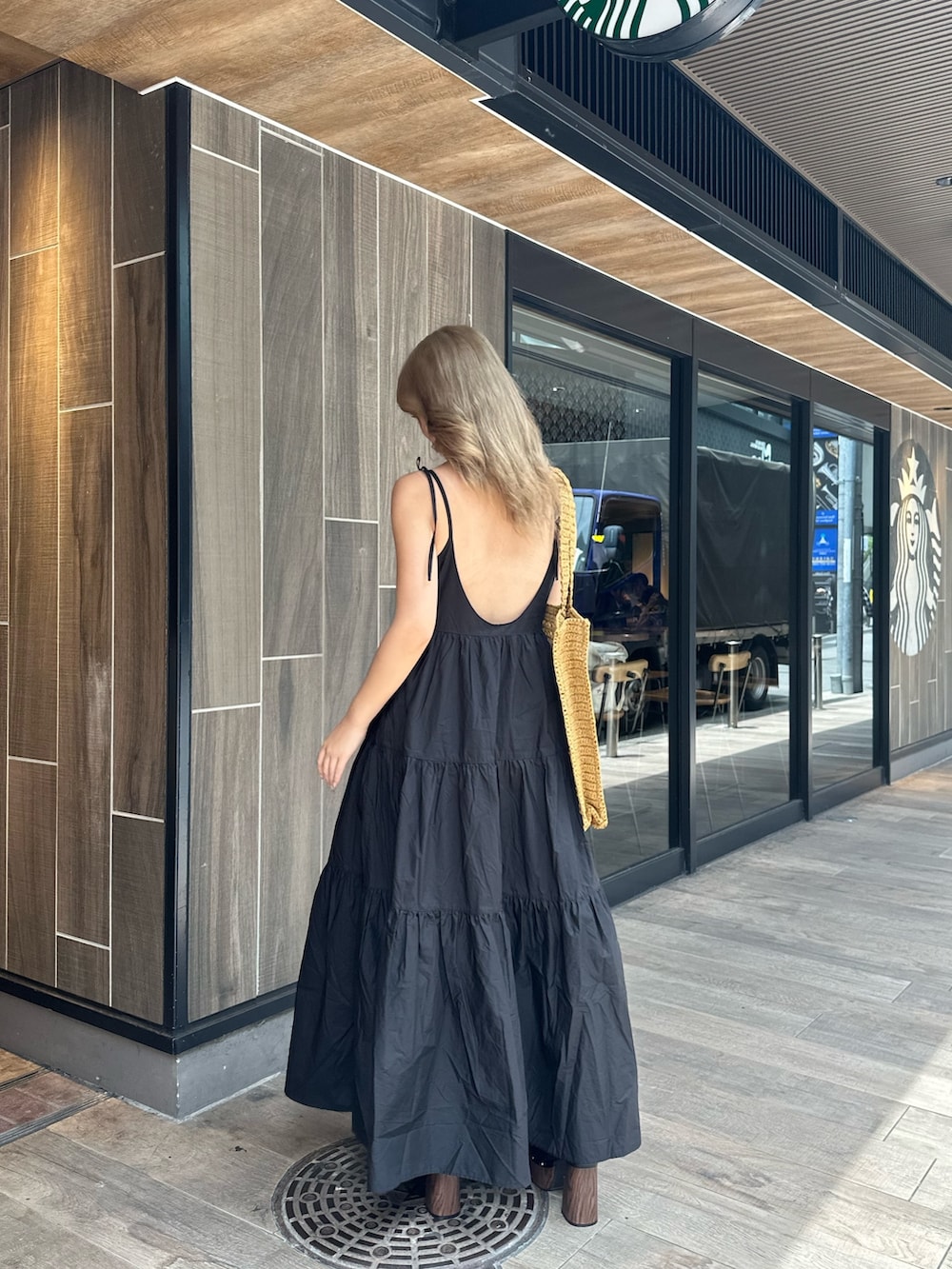 ブラック系のワンピース、ブラック系のサンダル、ベージュ系のトートバッグを着用したレディースの夏コーディネートの3枚目の写真