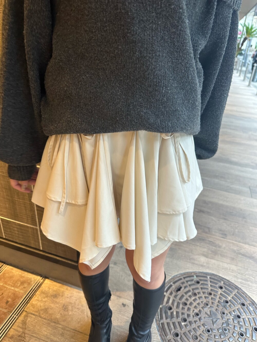 グレー系のワンピース、ホワイト系のスカート、ブラック系のブーツを着用したレディースの秋コーディネートの8枚目の写真