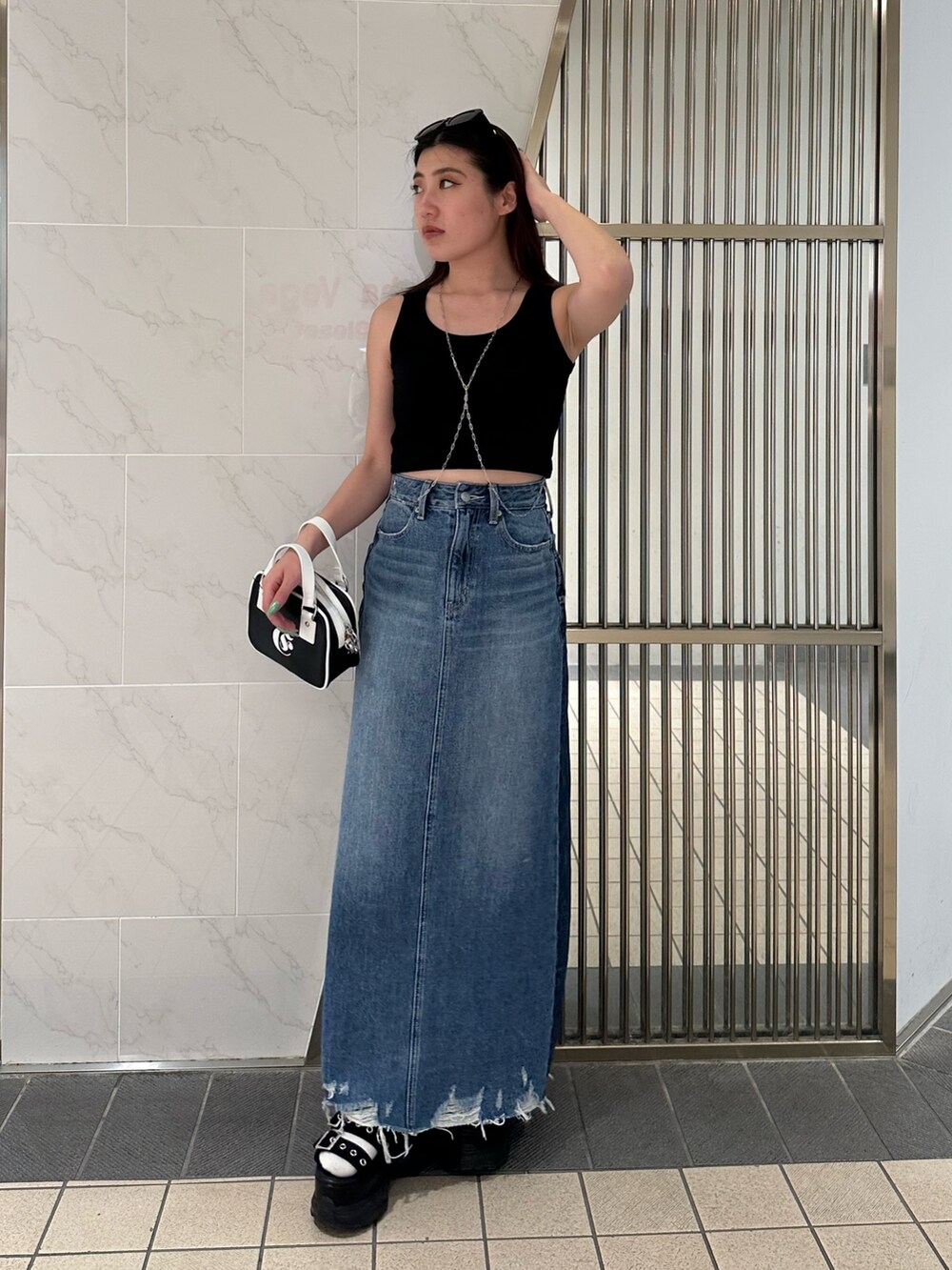 ブルー系のデニムスカート、ブラック系のタンクトップ、ブラック系のサンダルを着用したレディースの春コーディネートの2枚目の写真