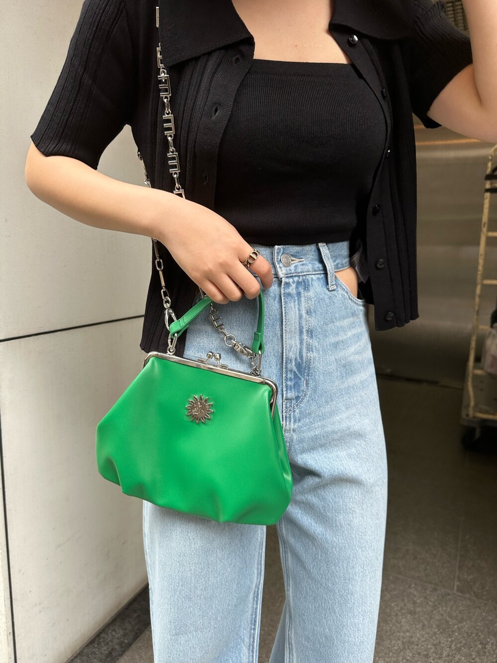 ブラック系のニット/セーター、ブルー系のデニムパンツ、グリーン系のショルダーバッグを着用したレディースの春コーディネートの6枚目の写真