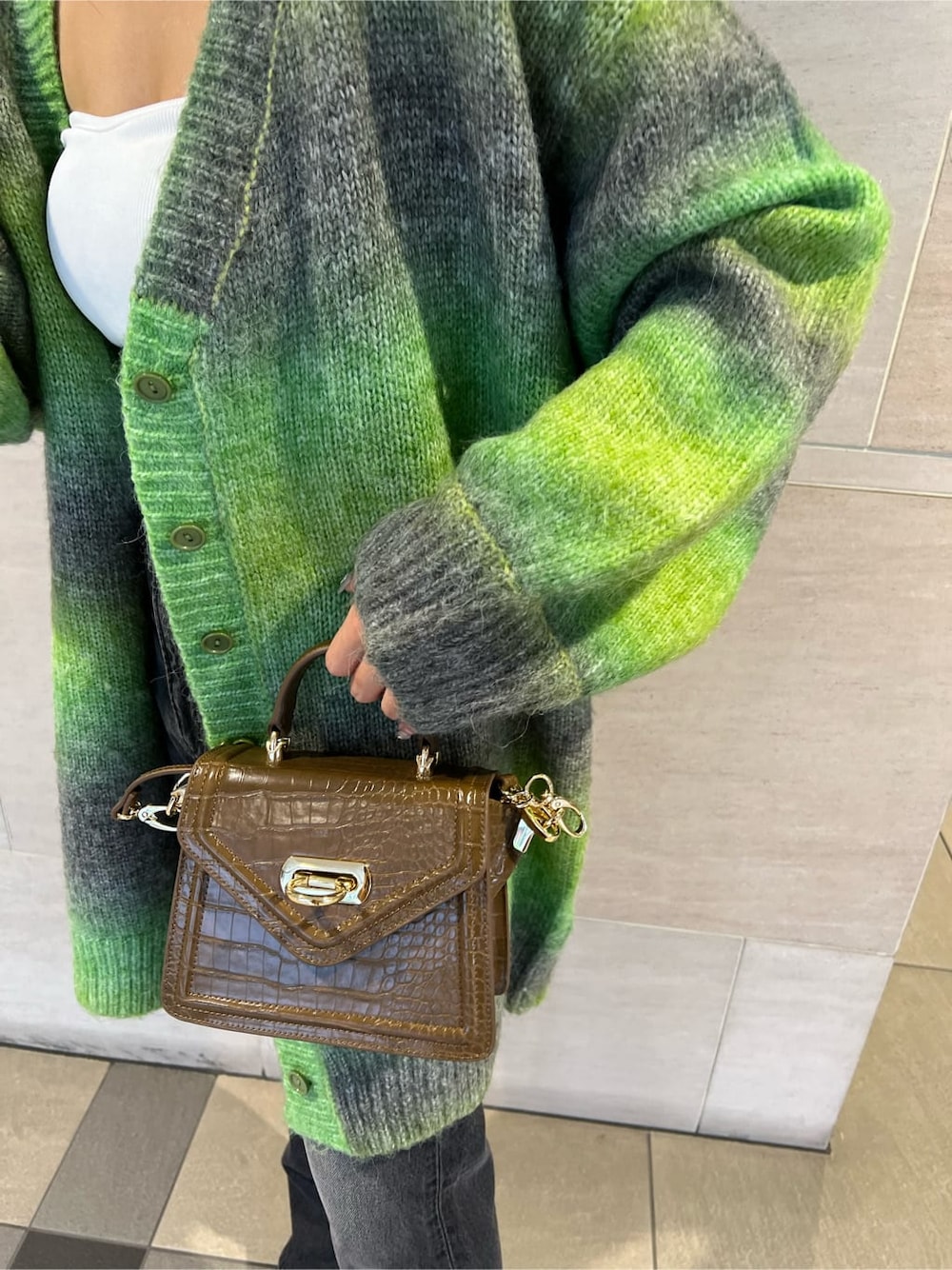 グリーン系のカーディガン/ボレロ、ホワイト系のチューブトップ、ブラック系のデニムパンツを着用したレディースの秋コーディネートの4枚目の写真