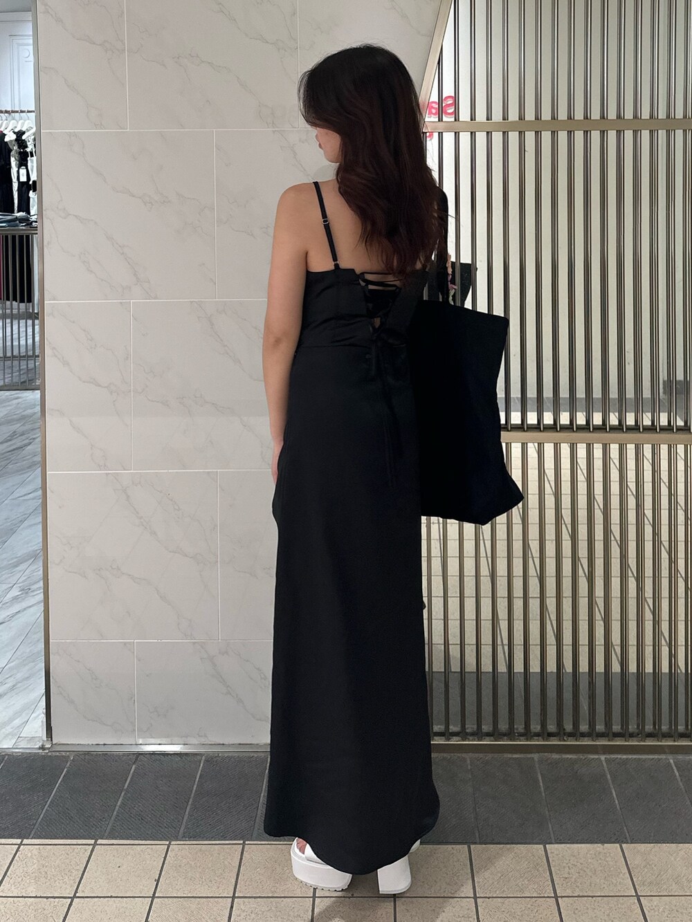 ブラック系のワンピース、ブラック系のトートバッグ、ホワイト系のサンダルを着用したレディースの夏コーディネートの4枚目の写真