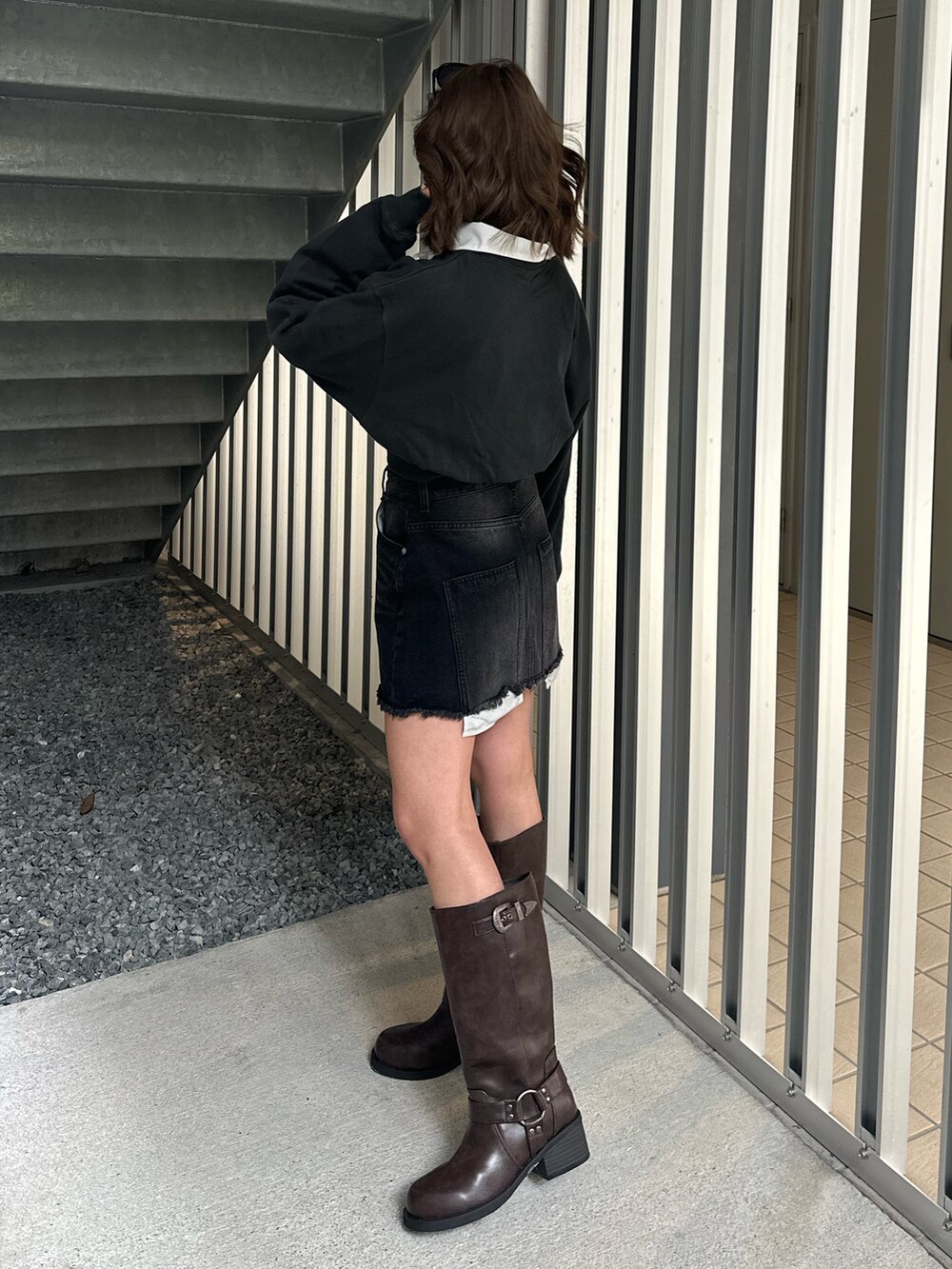 ブラック系のデニムスカート、ブラウン系のブーツ、ブラック系のスウェットを着用したレディースの冬コーディネートの2枚目の写真