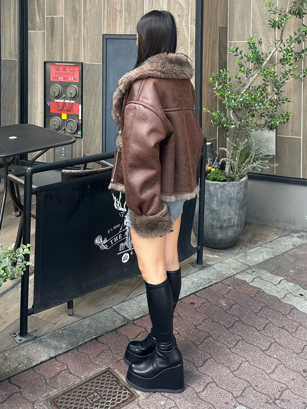 グレー系のワンピース、ブラウン系のブルゾン、ブラック系のブーツを着用したレディースの秋コーディネートの2枚目の写真