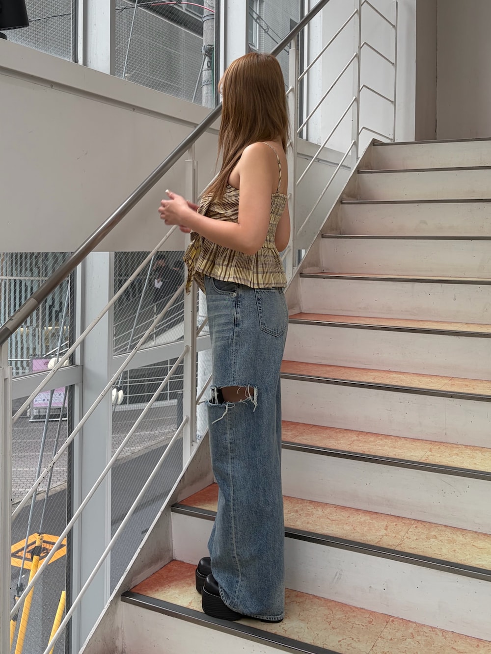 イエロー系のキャミソール、ブルー系のデニムパンツ、ブラック系のブーツを着用したレディースの夏コーディネートの2枚目の写真