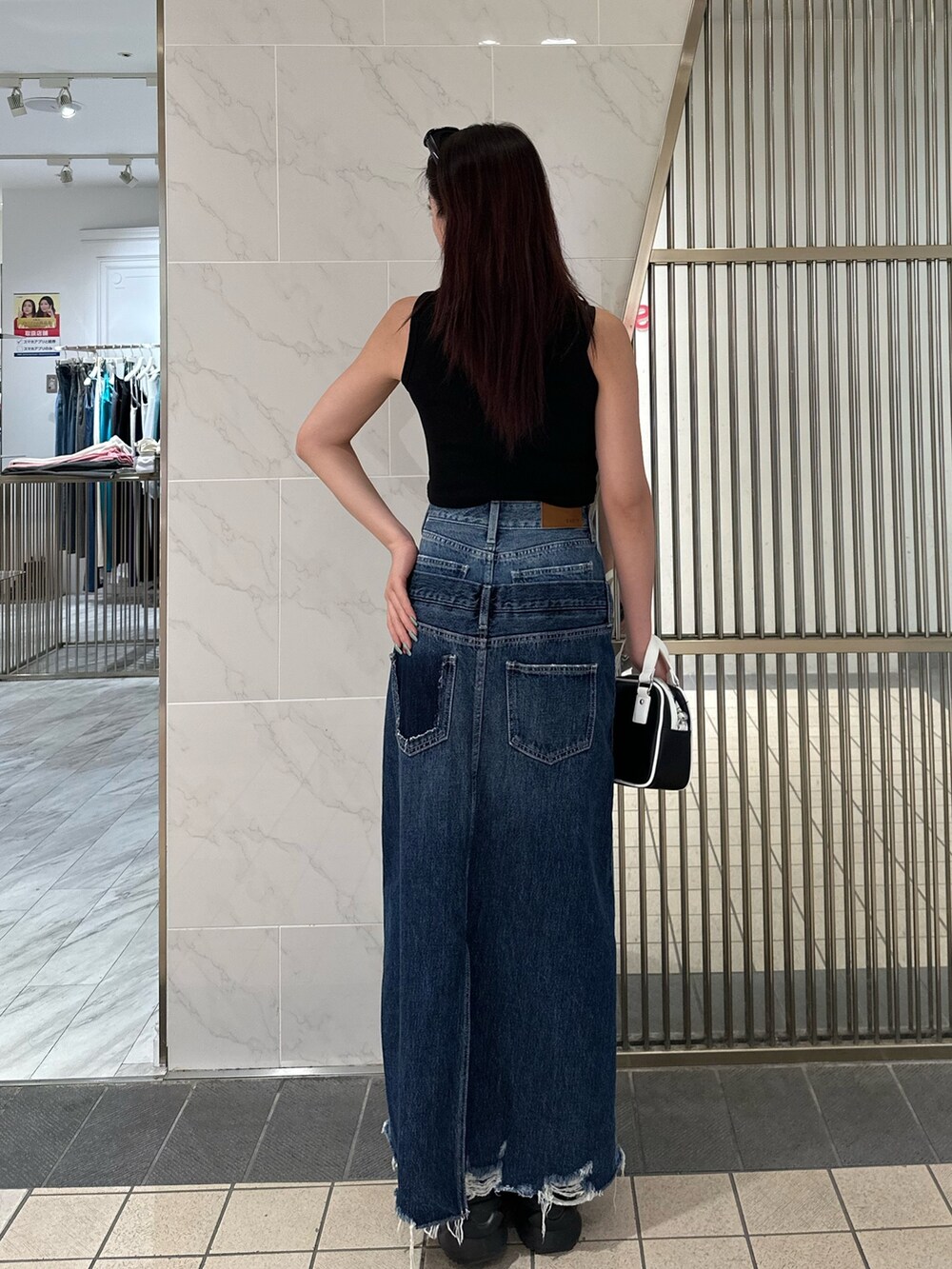 ブルー系のデニムスカート、ブラック系のタンクトップ、ブラック系のサンダルを着用したレディースの春コーディネートの4枚目の写真