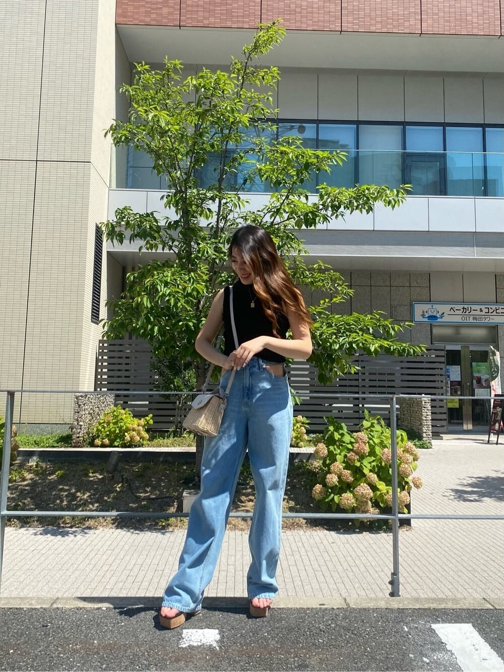 ブルー系のデニムパンツ、ブラック系のサンダル、ホワイト系のショルダーバッグを着用したレディースの夏コーディネートの2枚目の写真