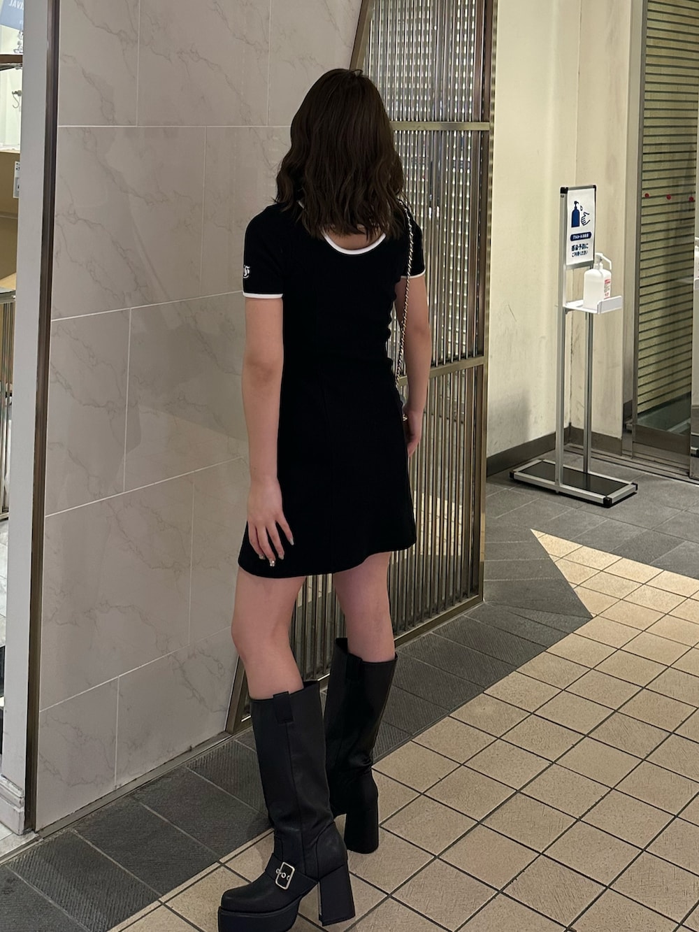 ブルー系のショルダーバッグ、ブラウン系のブーツ、ブラック系のワンピースを着用したレディースの春コーディネートの2枚目の写真