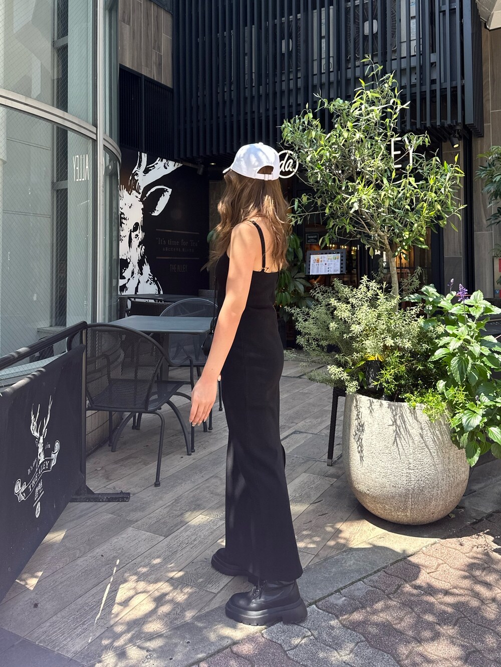 ブラック系のワンピース、ブラック系のブーツ、ホワイト系のキャップを着用したレディースの春コーディネートの2枚目の写真