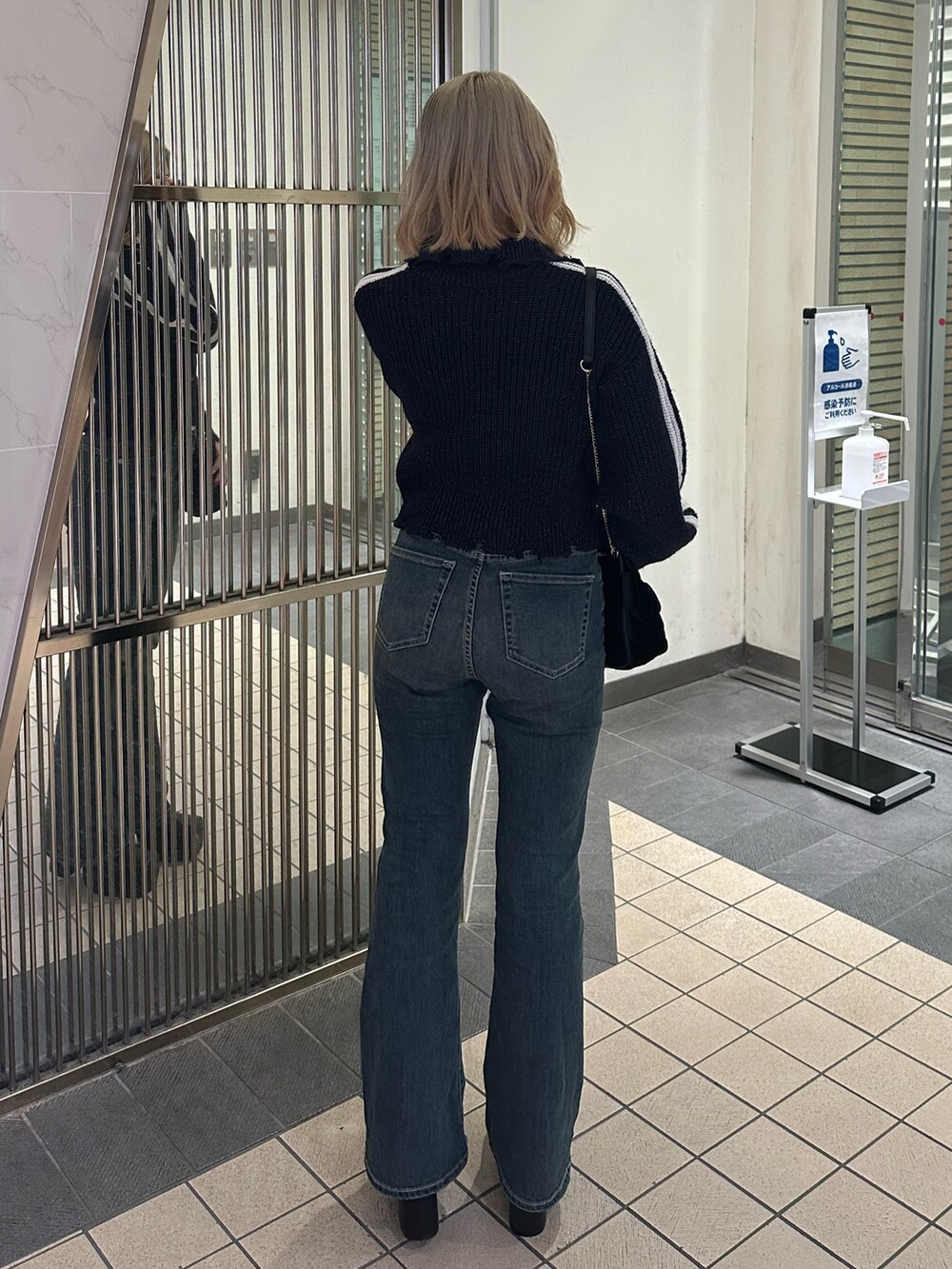 ブラック系のショルダーバッグ、ブルー系のデニムパンツ、ブラック系のブーツを着用したレディースの秋コーディネートの3枚目の写真